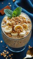 Delicious banana and granola parfait served in a glass with fresh mint leaves on a blue background photo