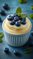 Creamy dessert topped with fresh blueberries and mint leaves on a textured blue surface photo