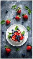 Fresh berry dessert presented on a white plate surrounded by strawberries and blueberries with mint leaves photo