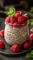 Delicious chia pudding topped with fresh raspberries and mint leaves served on a black plate photo