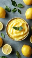 Fresh lemon sorbet served in a bowl surrounded by whole and sliced lemons and mint leaves on a grey surface photo
