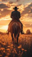 Cowboy riding a horse against a vibrant sunset in a golden field during late afternoon photo