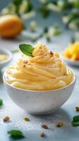 Creamy mango dessert topped with mint and crushed nuts served in a white bowl on a light blue surface photo