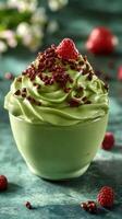 Bright green dessert topped with raspberry and crunchy red sprinkle served in a bowl on a textured surface photo
