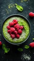 Vibrant green smoothie bowl topped with fresh raspberries and sesame seeds in a dark setting photo