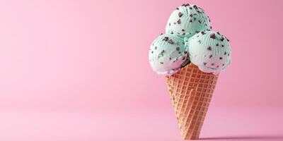 Mint chocolate chip ice cream cone with three scoops against a pink background at a summer dessert setting photo