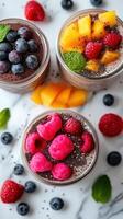 Colorful dessert jars filled with chia pudding topped with fresh fruits at a kitchen table photo