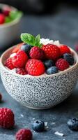Fresh berries served in a speckled bowl with mint and coconut flakes on a textured dark surface photo