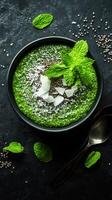 Healthy green smoothie bowl topped with coconut flakes and fresh mint leaves on a dark textured background photo