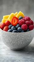 Fresh fruit salad with strawberries, blueberries, raspberries, pineapple, and black plate on a textured background photo