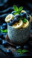 Healthy chia seed pudding topped with bananas and blueberries garnished with fresh mint leaves in a dark setting photo