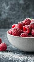 Fresh raspberries in a textured bowl with powdered sugar on a dark background photo