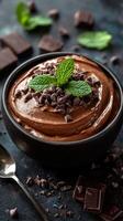 Delicious chocolate mousse topped with mint leaves and chocolate chips served in a dark bowl photo