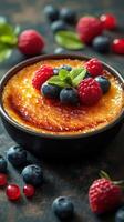 Delicious creme brulee topped with fresh berries and mint in a dark setting photo