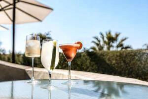 A variety of cocktails in different types of glasses on a glass-topped table. Midday happy hour time in tropical climate. Resort, holiday refreshment concept. photo