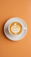 A cup of coffee with a leaf pattern on top of an orange background photo