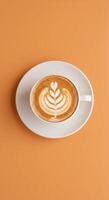 A cup of coffee with a leaf pattern on top of an orange background photo
