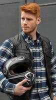 A man with red hair wearing a vest and holding a helmet photo