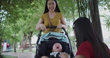 Handheld low angle view shot, Two young Asian women play with a little boy in a baby stroller outside a coffee shop. A relaxing atmosphere with a warm moment. video