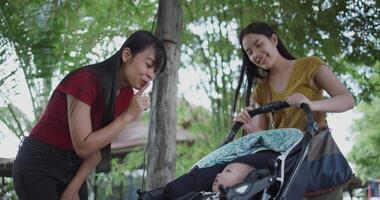 Handheld low angle view shot,Two young Asian women play with a little boy in a baby stroller outside a coffee shop. A relaxing atmosphere with a warm moment. video