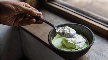 A hand holding a s scooping a sful of creamy yogurt from a bowl with visible cultures and textures evoking the homemade fermentation experience.. photo