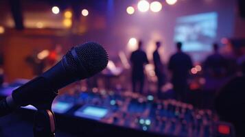 Closeup of a handheld microphone in the foreground with blurred figures of crew members in the background as they communicate and finetune the sound setup before the live event begins photo