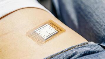 A closeup view of a dermal patch adhered to the skin embedded with microfluidic sensors that analyze sweat composition to track hydration and electrolyte levels. The patchs. photo