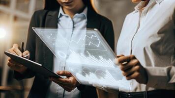A midair holographic display showing predictive analytics for customer trends with a focused team member taking notes on a digital tablet beside it.. photo