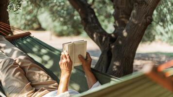 Senior man relaxing in hammock reading a book under olive tree photo