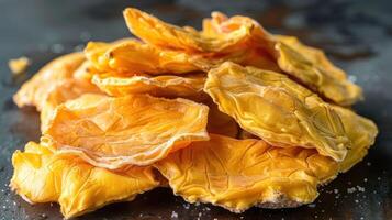 A close-up of dried mango slices arranged on a dark surface. photo