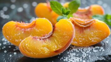 Juicy peach slices sprinkled with salt and garnished with mint on a dark surface. photo