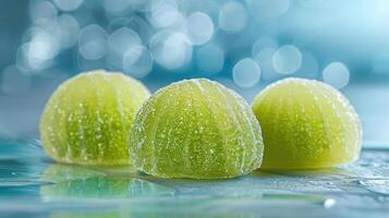 Three sparkling green candies glisten on a reflective surface against a blurred background. photo