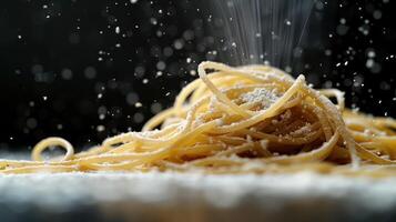 A close-up of spaghetti being sprinkled with powdered cheese against a dark background. photo