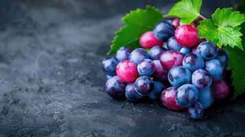 A cluster of colorful grapes with leaves on a dark textured surface. photo