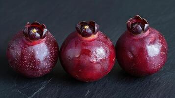 Three glossy, dark red fruits displayed on a slate surface. photo