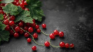 A close-up of fresh red currants with green leaves on a dark textured surface. photo