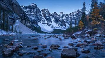 Serene mountain landscape with a lake, rocky shore, and snow-capped peaks at dusk. photo