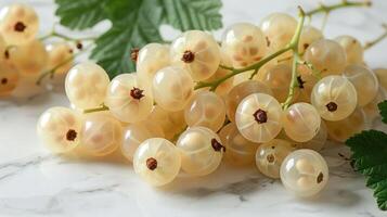 A cluster of pale yellow currants resting on a marble surface with green leaves. photo