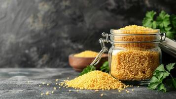 A jar of yellow grains with a bowl nearby, surrounded by fresh herbs on a textured surface. photo