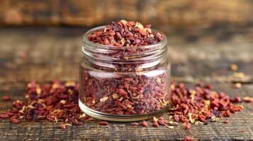 A jar filled with dried red spices, surrounded by scattered bits on a wooden surface. photo