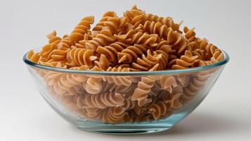 A glass bowl filled with uncooked spiral pasta, showcasing its texture and color. photo