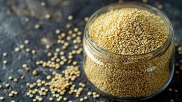 A glass jar filled with quinoa seeds, with some scattered on a dark surface. photo