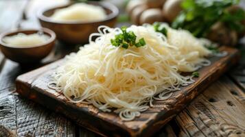 A serving of cooked rice noodles garnished with green onions on a wooden board. photo