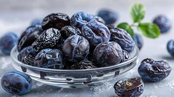 A bowl of fresh and dried plums on a textured surface, highlighting their rich color. photo