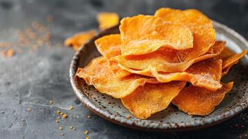A close-up of crispy, golden-orange mango chips on a textured plate. photo
