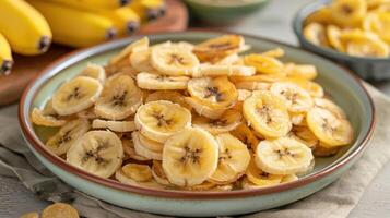 A bowl of dried banana slices with fresh bananas in the background. photo