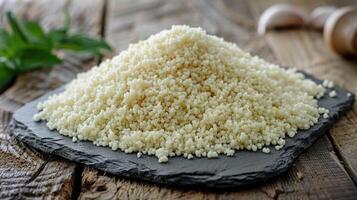 A mound of uncooked couscous on a slate surface, ready for cooking or culinary use. photo