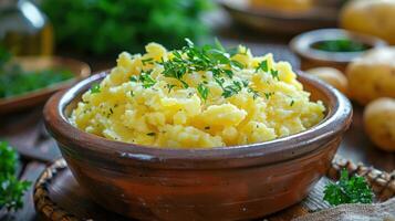 A bowl of creamy mashed potatoes garnished with herbs, set in a rustic kitchen environment. photo