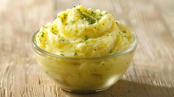 A bowl of creamy mashed potatoes garnished with herbs, served on a wooden surface. photo