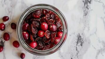 A jar filled with dried cranberries and fresh cranberries on a marble surface. photo